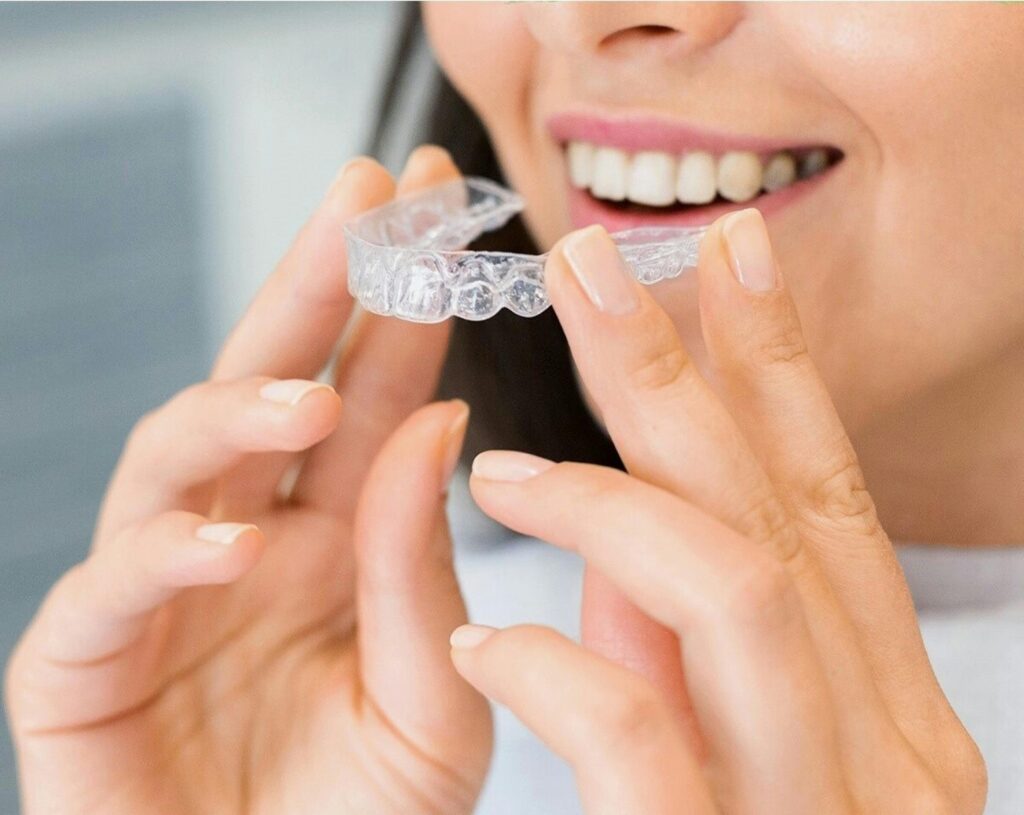 Close-up of a woman holding a Invisalign clear dental aligner, showcasing dental health and a bright smile.